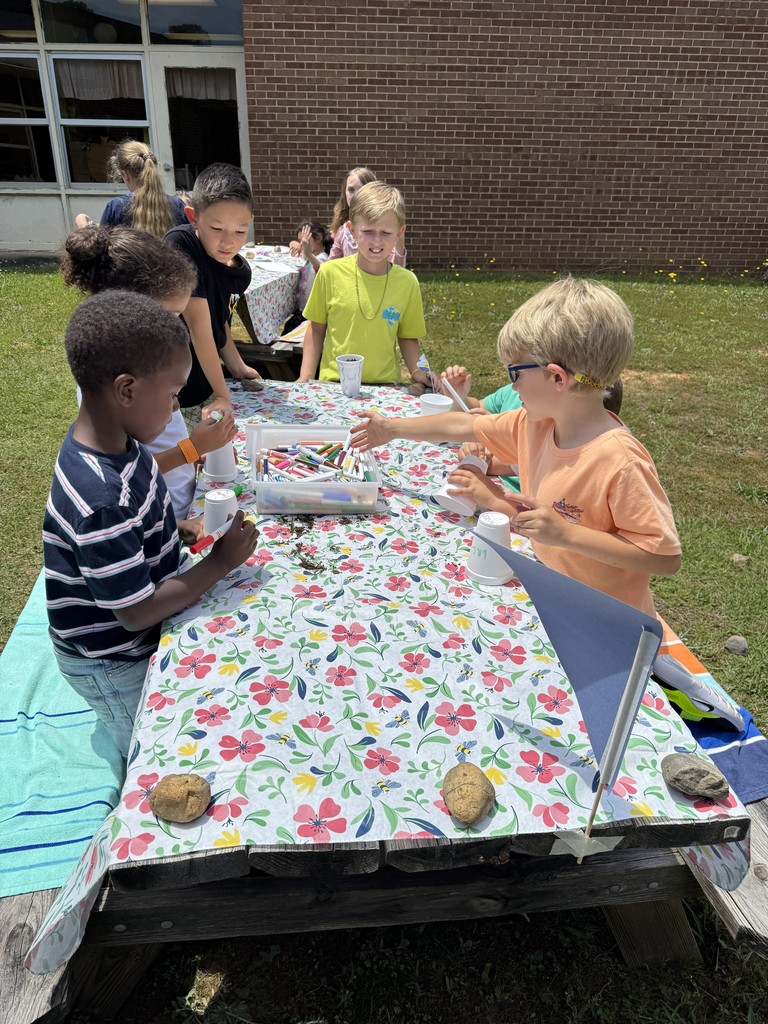 Fourth grade students look on in the Bryan garden as kindergarten students work on a garden craft using paper cups.