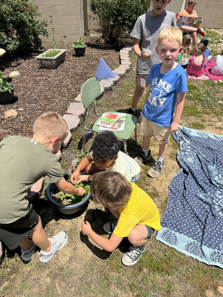 Kindergarten students work with a potted plant in the Bryan garden. A fourth grade student guides them.