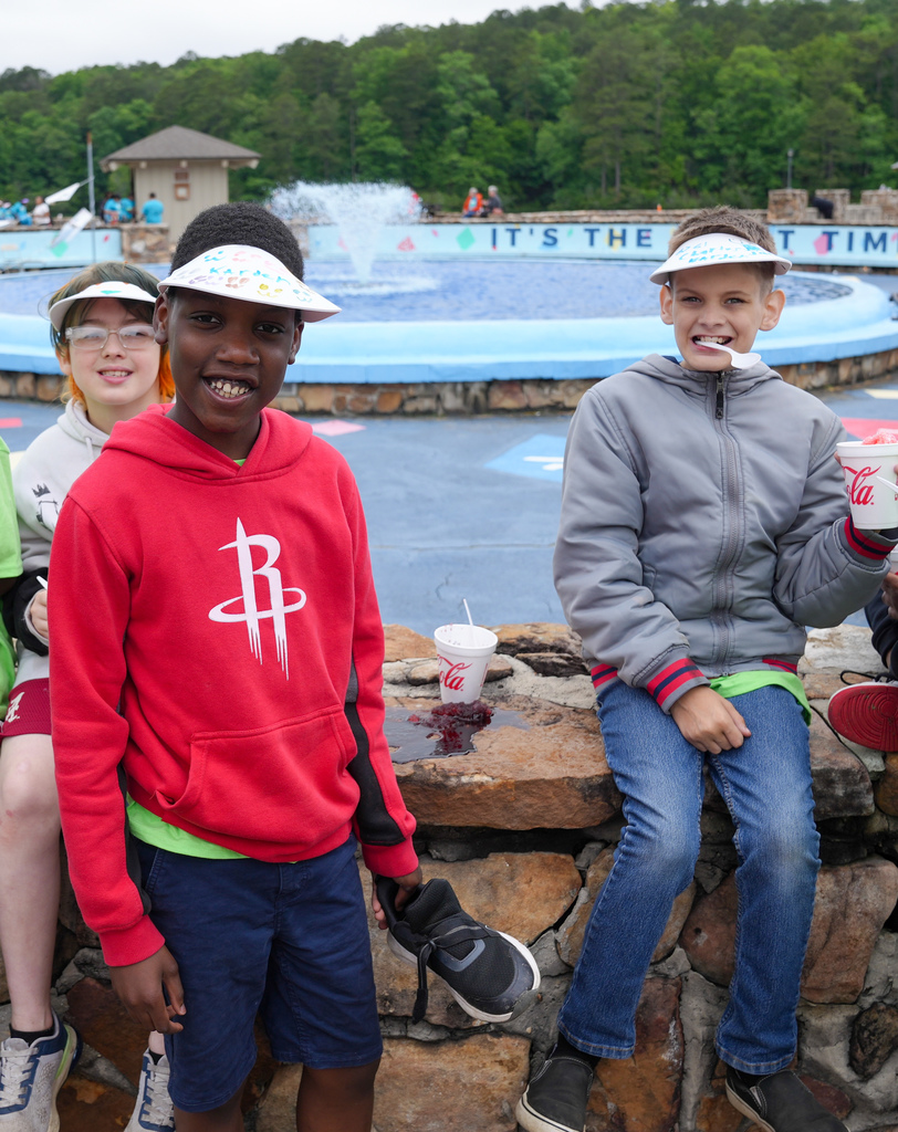 Students sit outside a fountain at Oak Mountain State Park. They smile at the camera while eating snow cones.