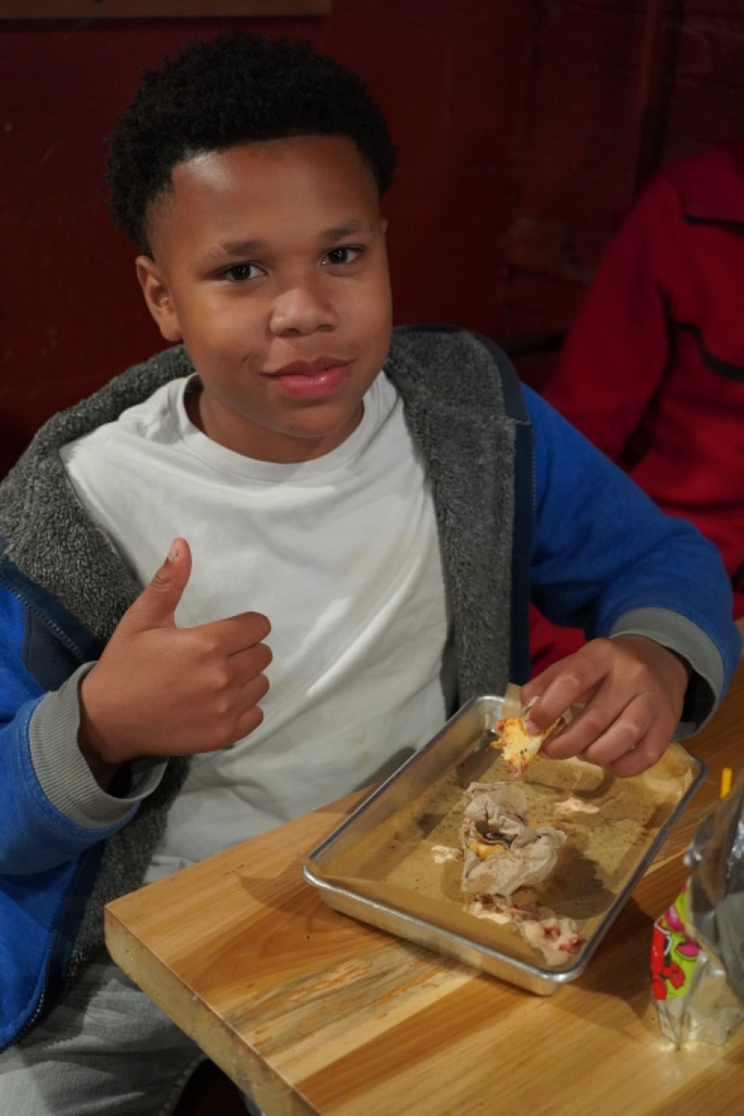 A boy gives a thumbs up while eating a meal at a restaurant .