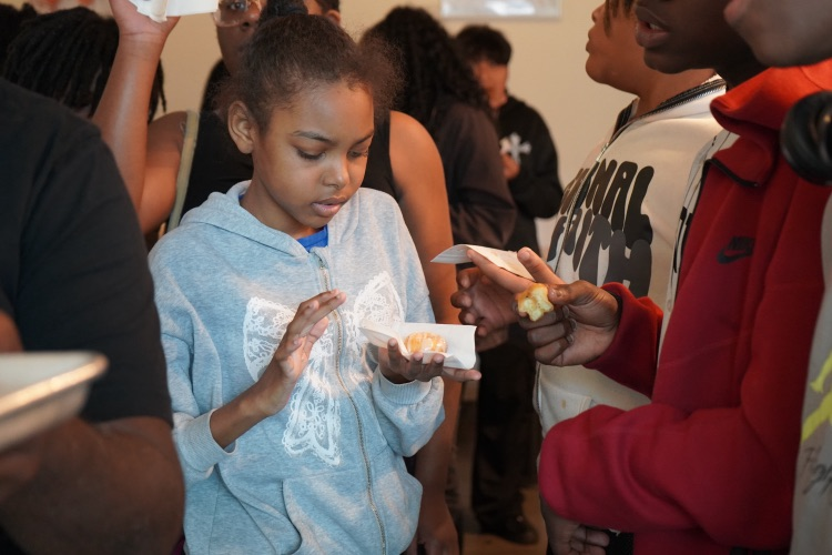A girl holds a small donut while standing inside a bakery.