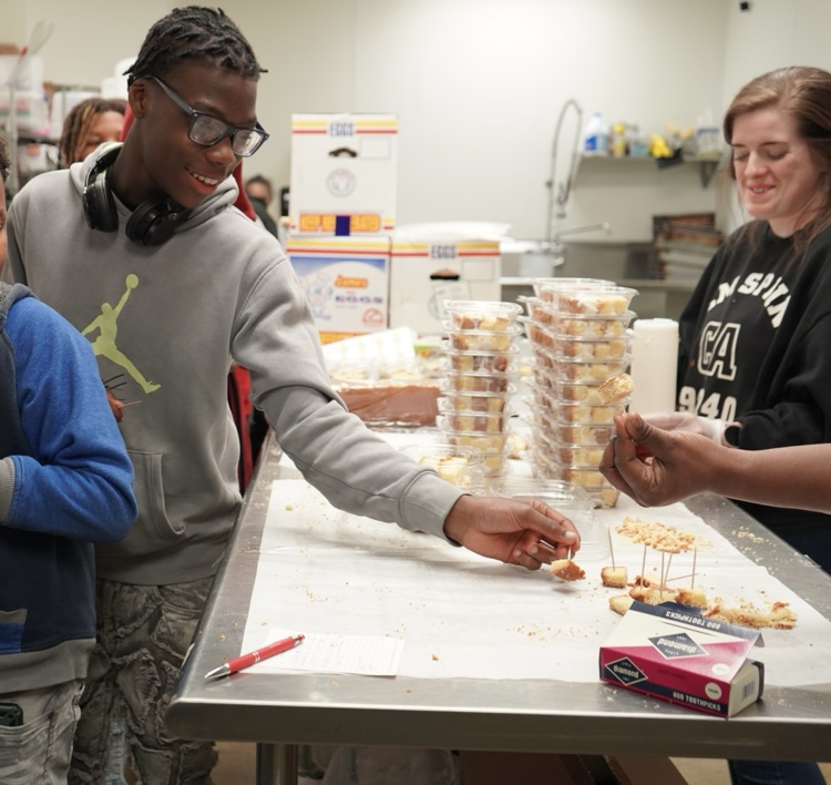 Students reach for pieces of pound cake on a table at a bakery.