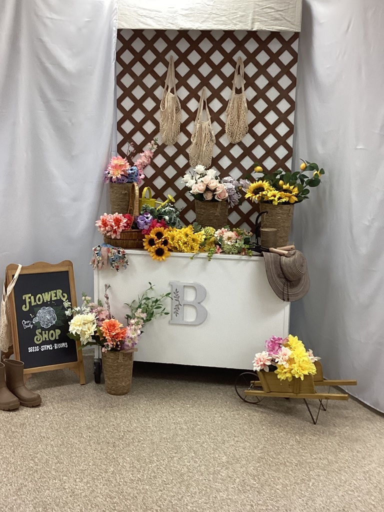 Arrangements of spring flowers decorate a linen covered table with the letter B in front. A chalkboard flower shop sign is in front of the table.