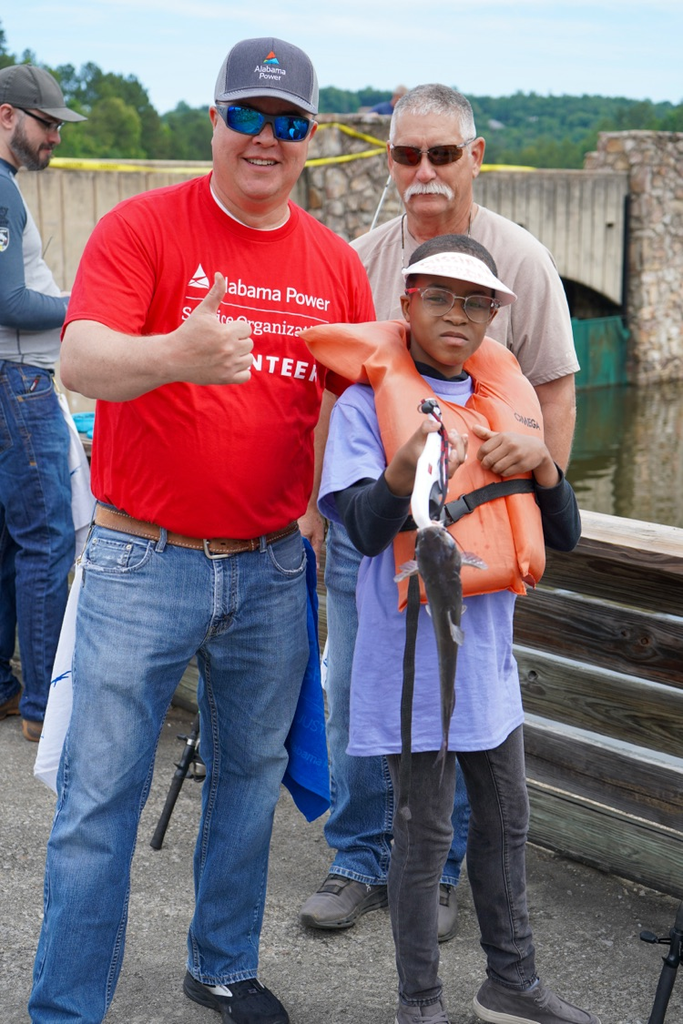 A man and a child pose together for a photo on a fishing pier. The child holds a catfish in his hand.