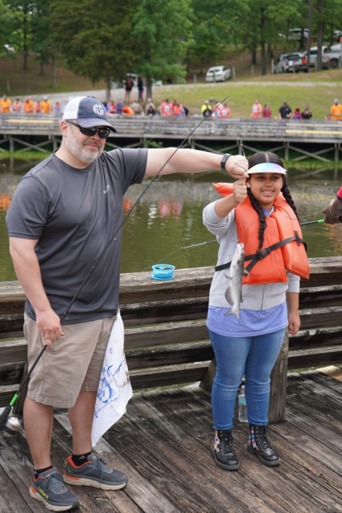 A girl and man stand on a fishing pier and smile. They hold up a catfish with their hands.