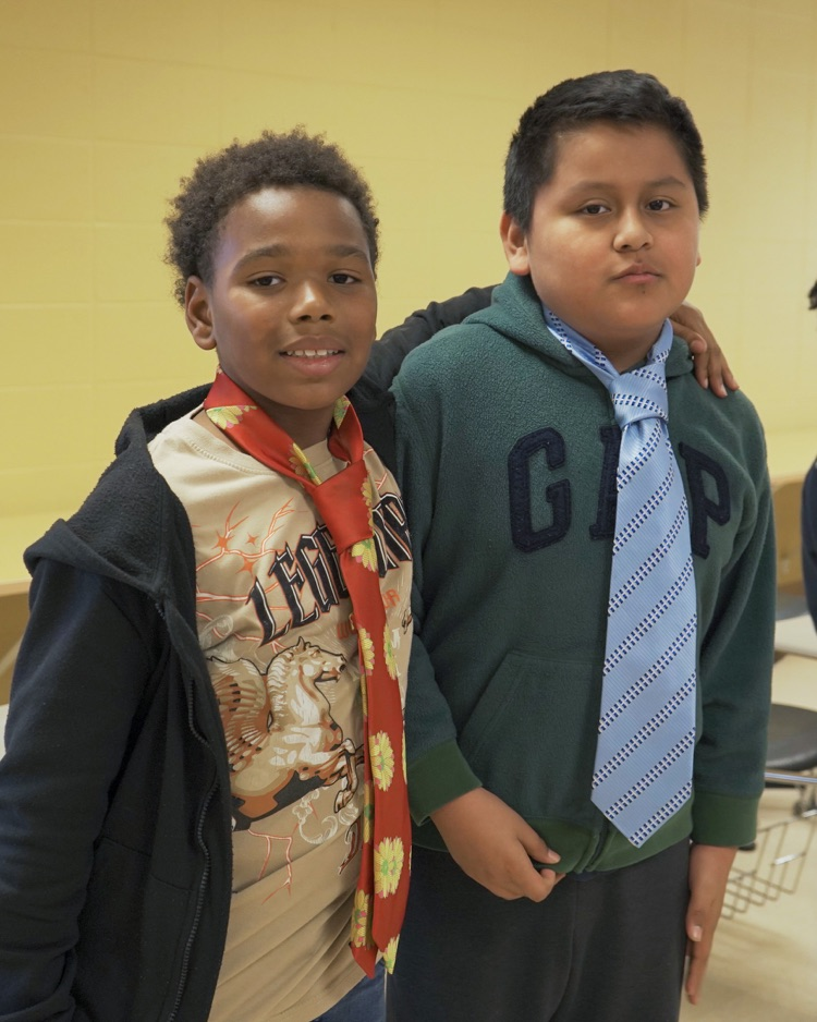 Two boys smile for a photo. They wear ties over their clothes.