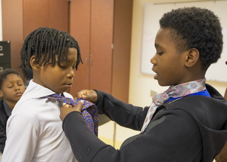 A boy helps another boy tie a tie  
