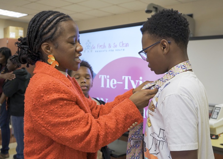 A woman ties a tie for a  boy. 