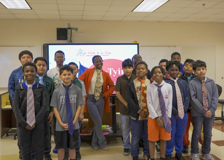 A group of students and an adult stand together for a photo and smile. They all wear ties over their clothes.