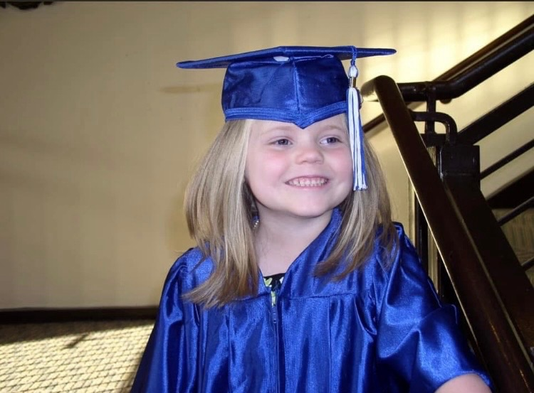 A girl smiles while standing on a staircase. She wears a cap and gown.