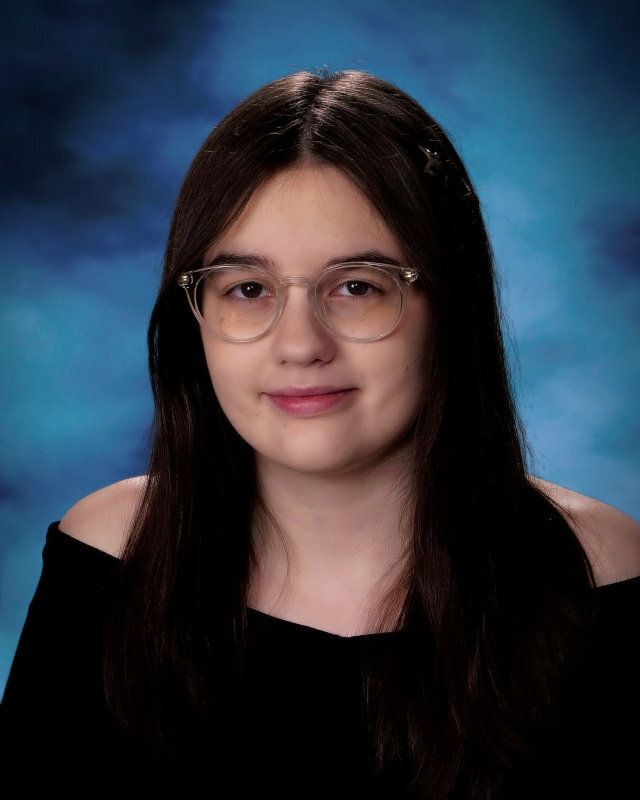 Keira Michelle Duncan wears a black top and smiles while standing in front of a blue background.