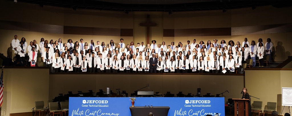 Graduates participating in JEFCOED's White Coat Ceremony stand together in the balcony of a church for a photo. Superintendent Dr. Walter Gonsoulin stands in the middle of them.