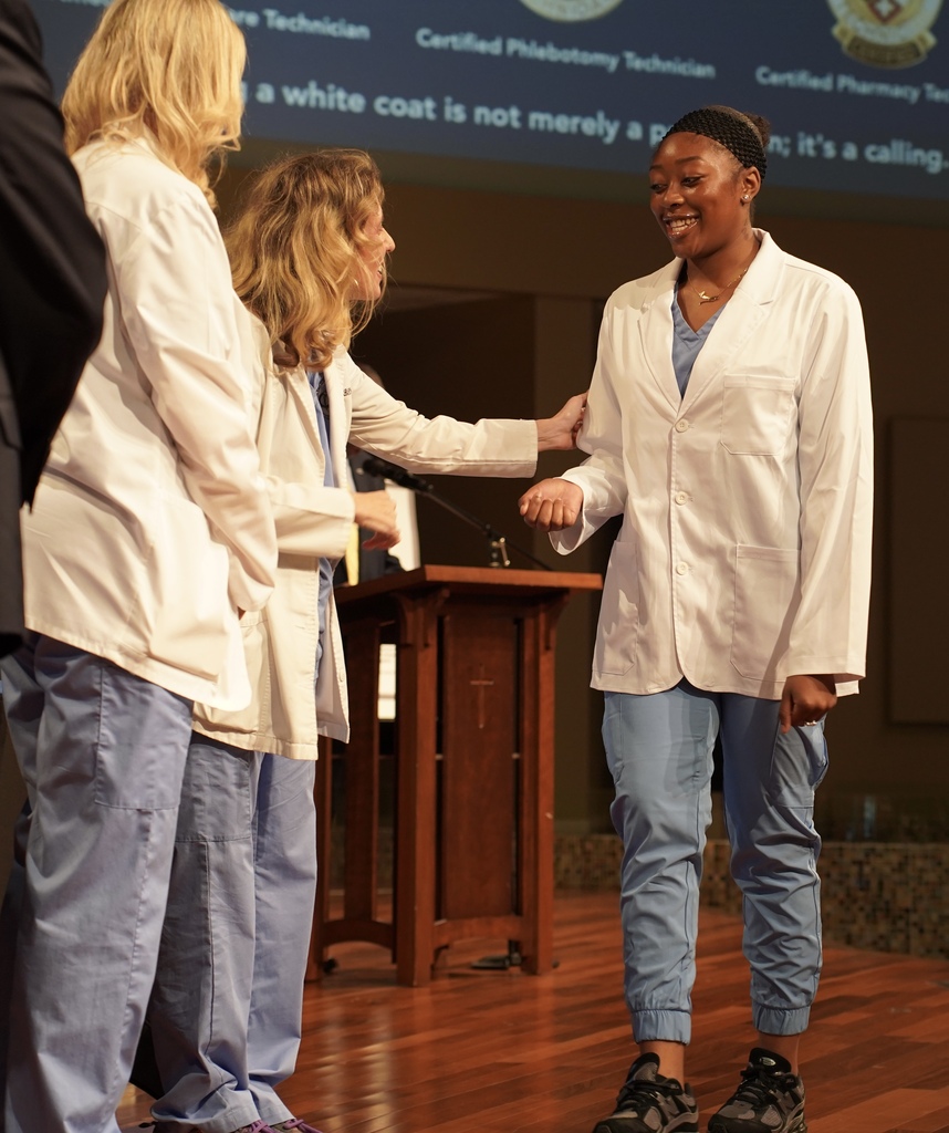 A girl smiles while walking across the stage during the JEFCOED White Coat Ceremony.