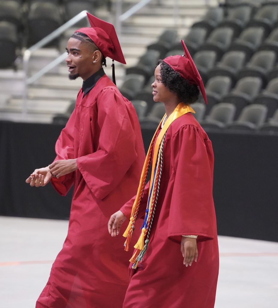 Students wearing caps and gowns walk down the floor of a room during the Shades Valley High School graduation ceremony.