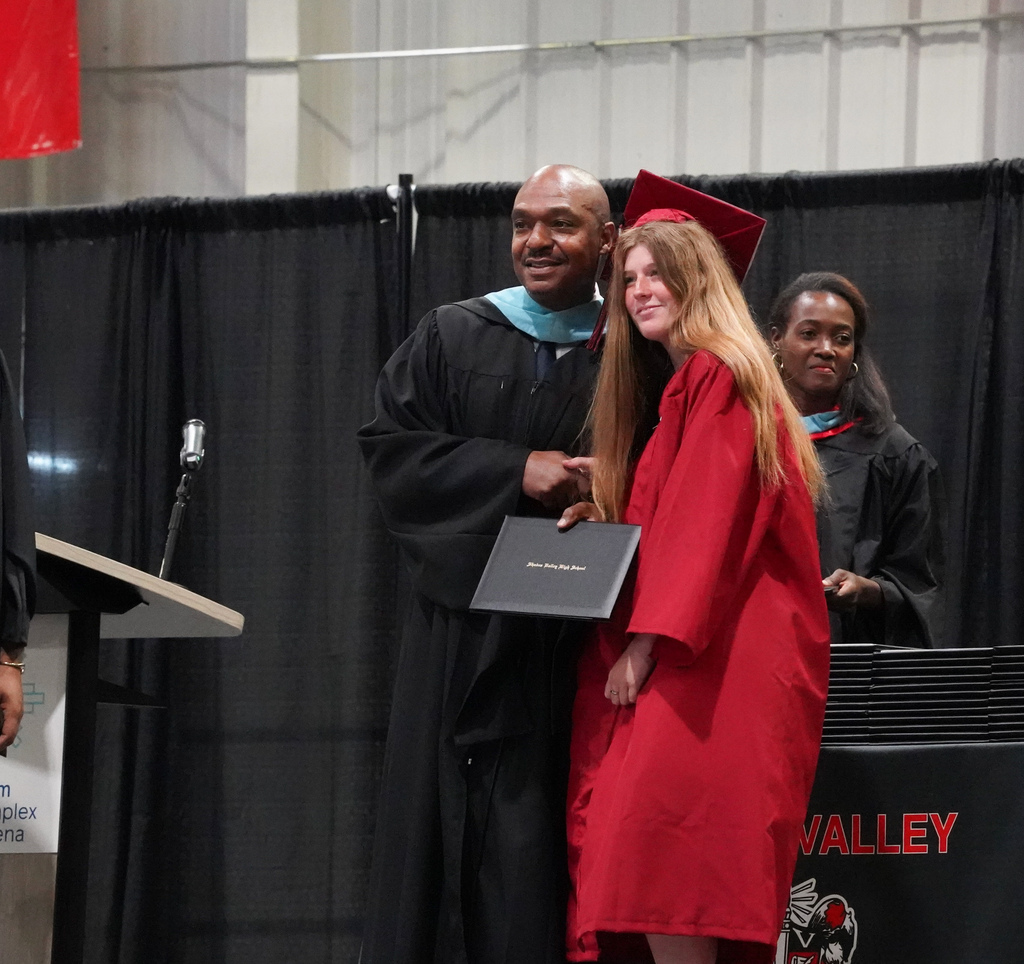 A girl and the Shades Valley High School principal take a photo together on stage during the school's graduation ceremony.