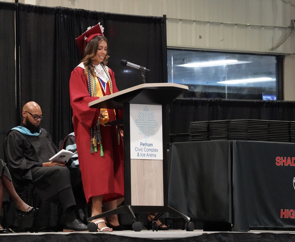 A girl wearing a cap and gown speaks into a microphone during the Shades Valley High School graduation ceremony.