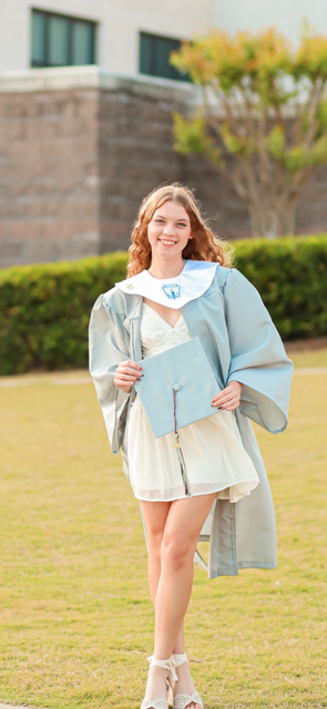 Evie Grace Holmes smiles for a graduation photo. She wears a blue gown and holds a blue cap in her hands.