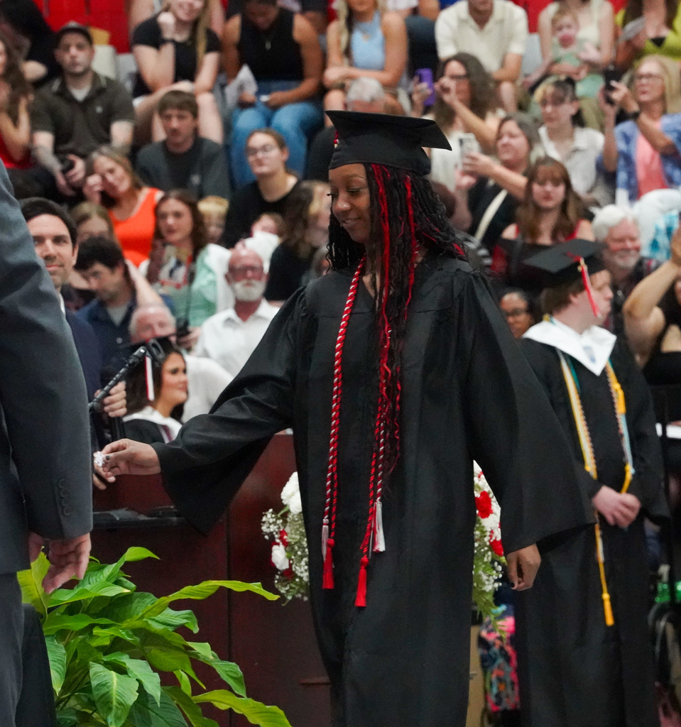 A student wearing a cap and gown walks to receive her diploma during the Oak Grove High School graduation ceremony.