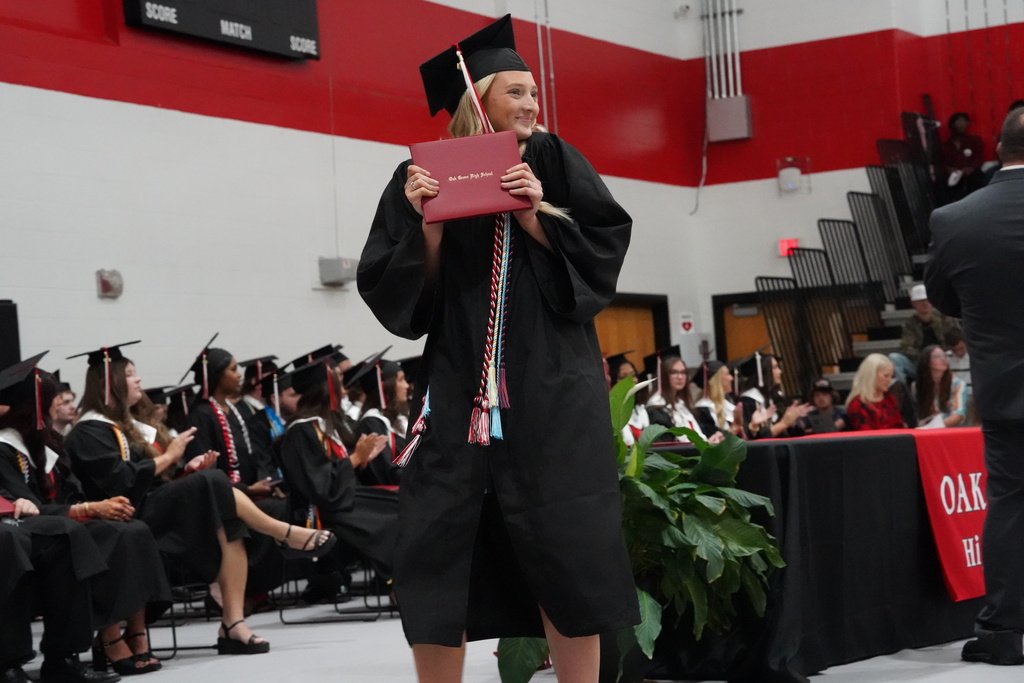 A student smiles and holds her diploma during Oak Grove High School's graduation ceremony.