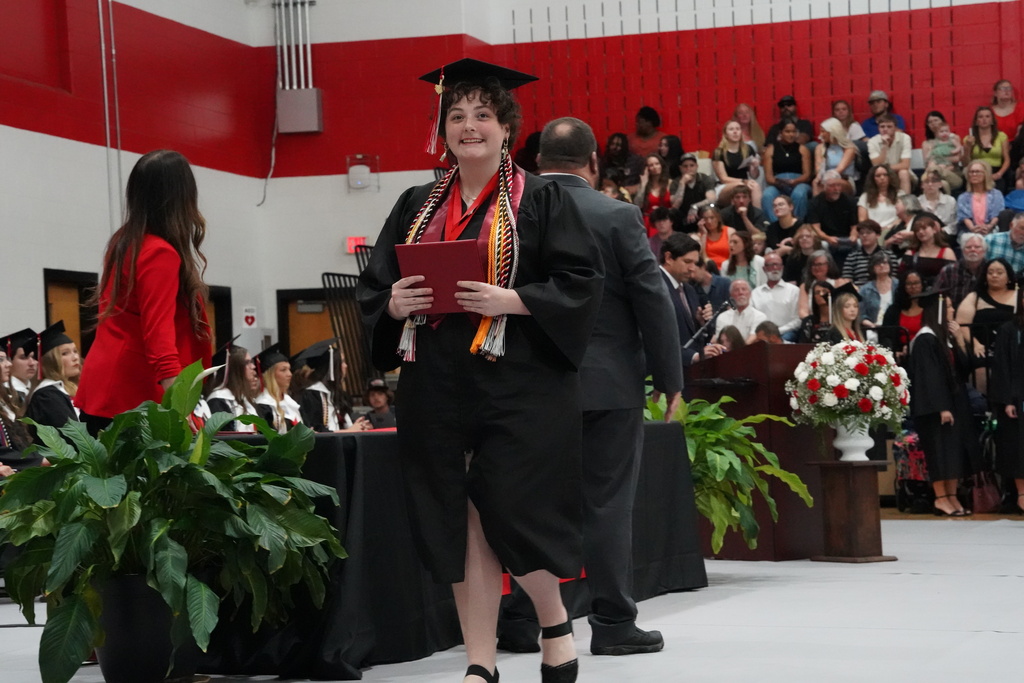 A student smiles and holds a diploma while wearing a cap and gown during Oak Grove High School's graduation ceremony.