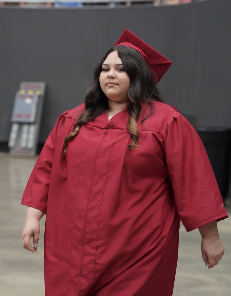 A student wearing a red cap and gown enters the auditorium for her high school graduation ceremony.