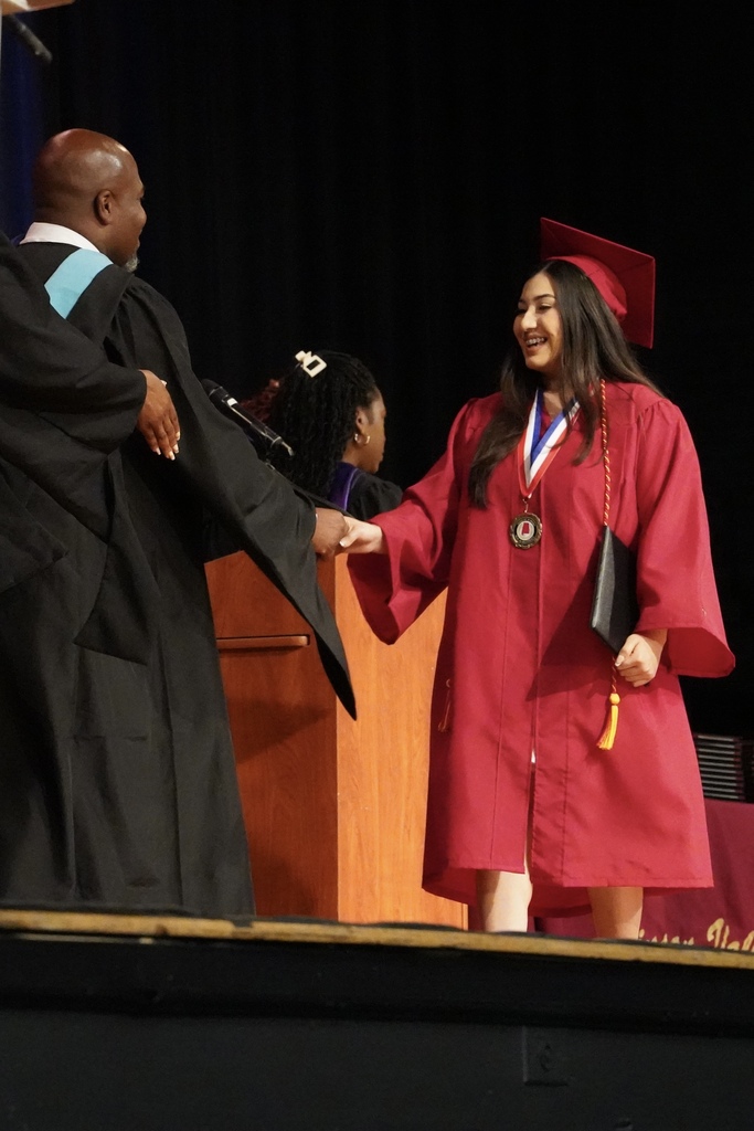 A student smiles while shaking a man's hand on stage at a graduation ceremony.