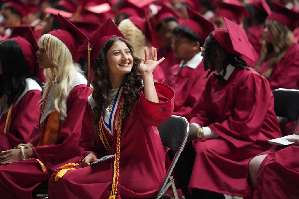 A student wearing a red cap and gown smiles and waves during the Pinson Valley High School graduation ceremony.