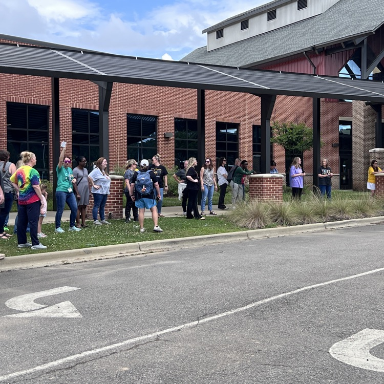 group of teachers waving goodbye to students as the buses roll out on the last day of school