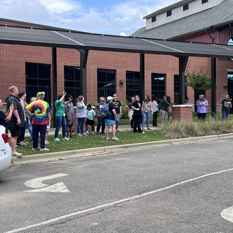 group of teachers waving goodbye to students as the bus rolls out on the last day of school