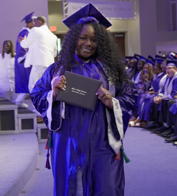 A Minor High School graduate smiles and holds up her diploma during the school’s graduation ceremony.