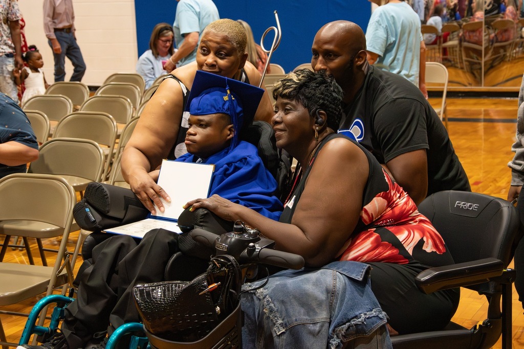 Loved ones surround a Burkett Center graduate for a photo following the Burkett Center graduation ceremony. The student wears a blue cap and gown.