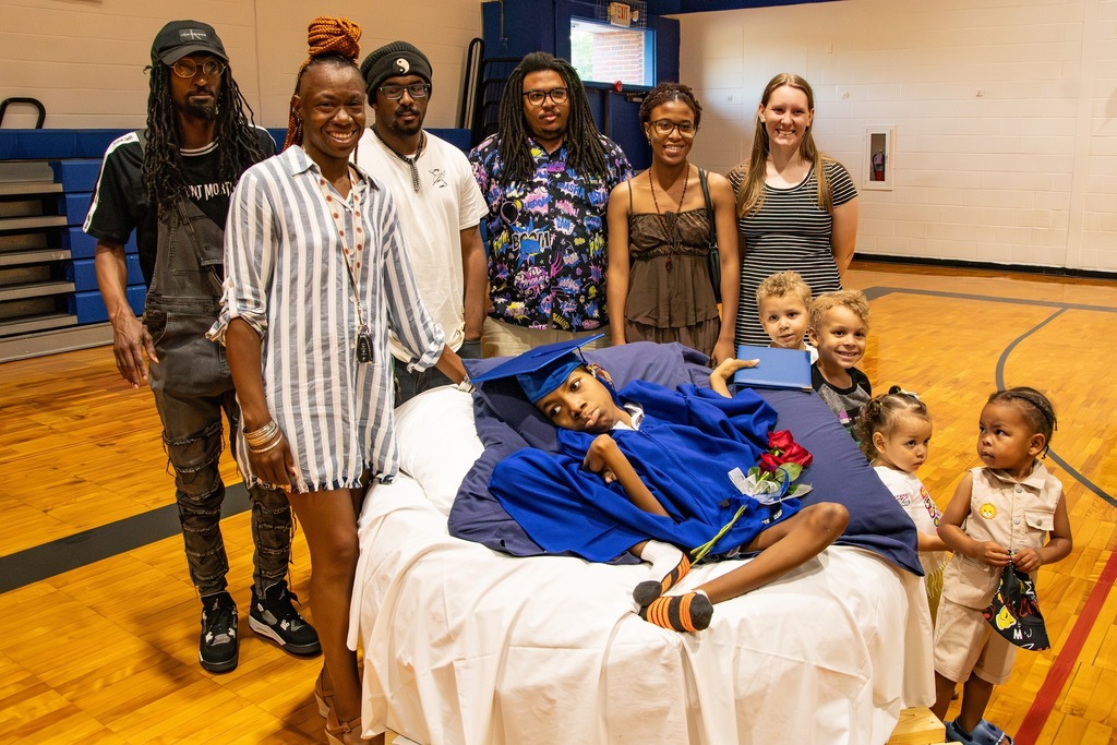Loved ones surround a Burkett Center student for a photo following the school's graduation ceremony. The student lays on a round white cushion.