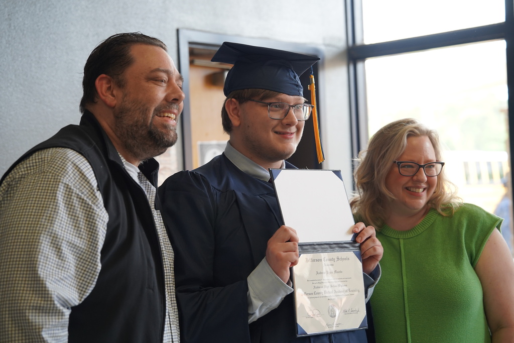 A JCVAL student smiles and holds up his diploma while posing for a photo with his loved ones.