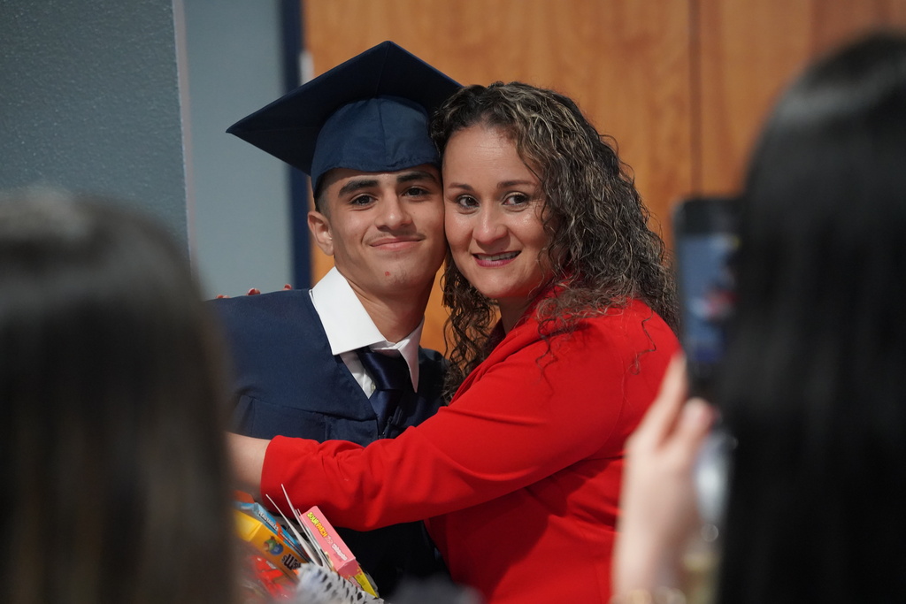 A woman and a JCVAL graduate smile for a photo following the school's graduation ceremony. The student wears a blue cap and gown.