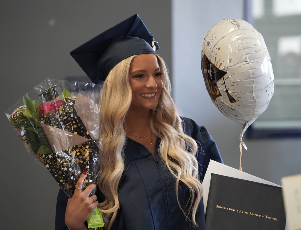 A JCVAL student smiles for a photo following the school's graduation ceremony. She holds a balloon and flowers and wears a blue cap and gown.