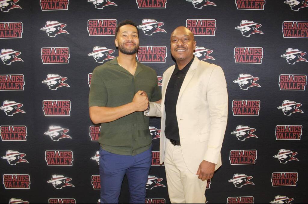 Taki Sarhaan poses for a photo with a man during his retirement party. He stands in front of a Shades Valley High School photo backdrop.
