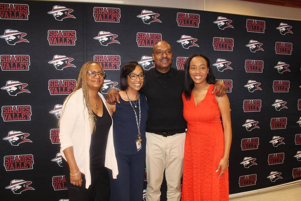Shades Valley High School Principal Taki Sarhaan poses for a photo with three women. They stand in front of a Shades Valley High School photo backdrop.