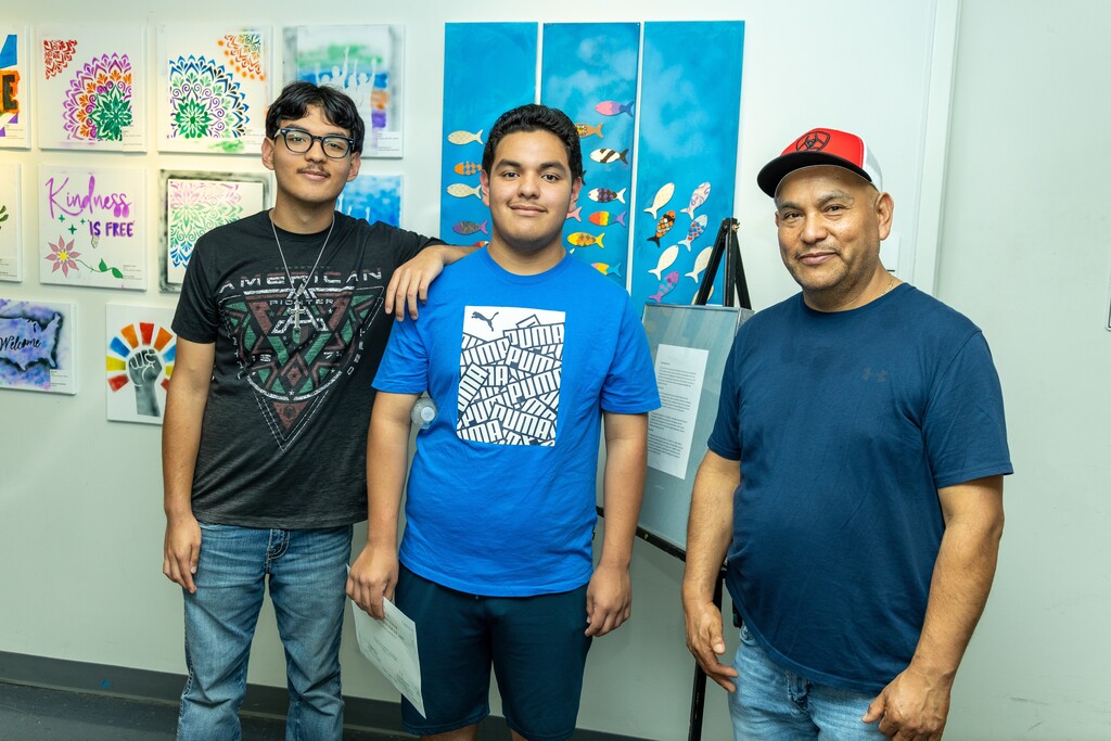 Two young men and an older man stand together for a photo. They pose in front of hand-drawn art on display at the Birmingham Museum of Art.
