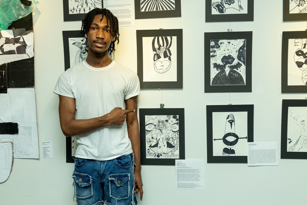 A student smiles and points to drawings hanging on a wall.
