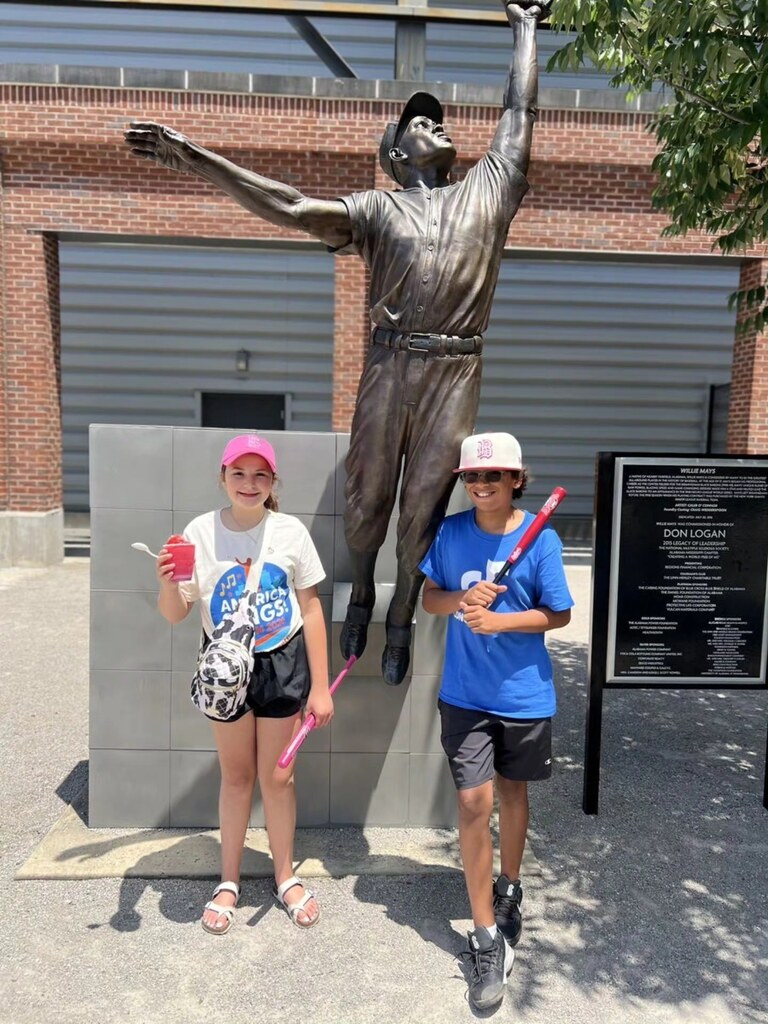 Two Concord Elementary School choir students stand for a photo outside Regions Field and smile. They pose in front of a statue of a baseball player.