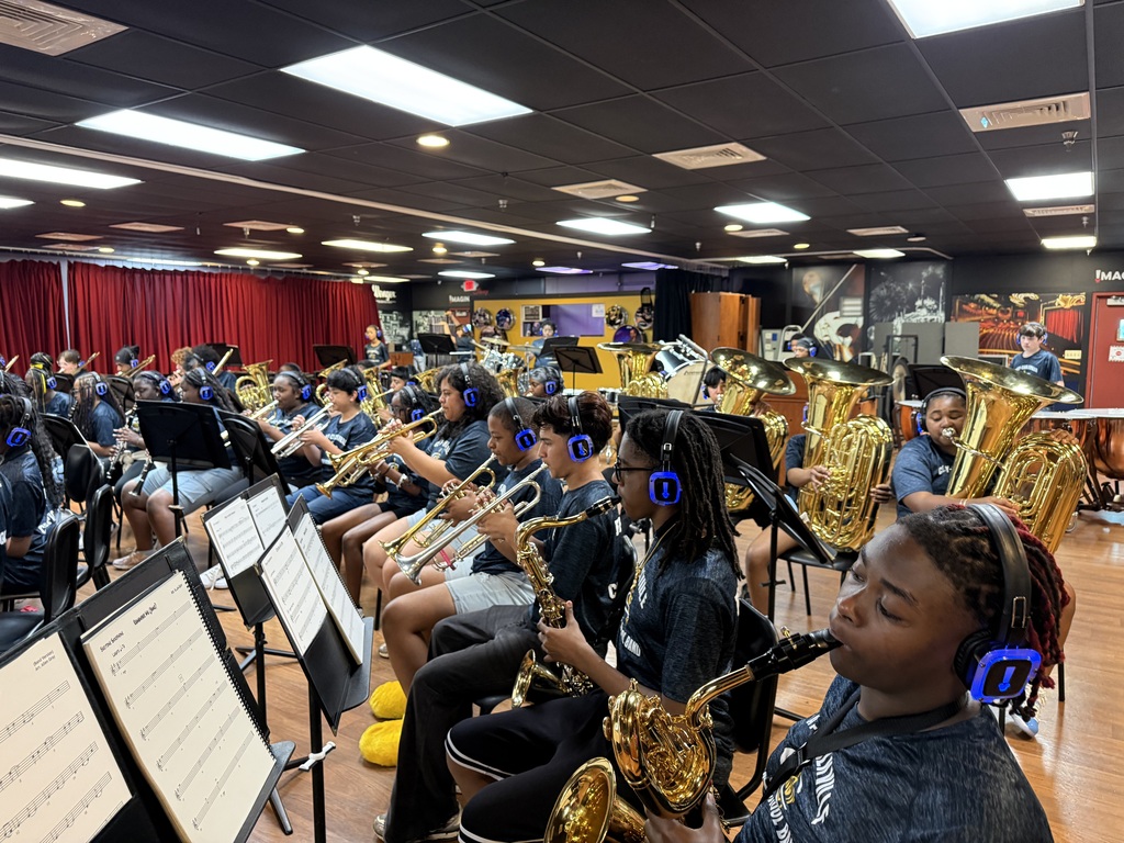 Clay-Chalkville Middle School students sit in a room and play instruments. They play sitting behind music stands.