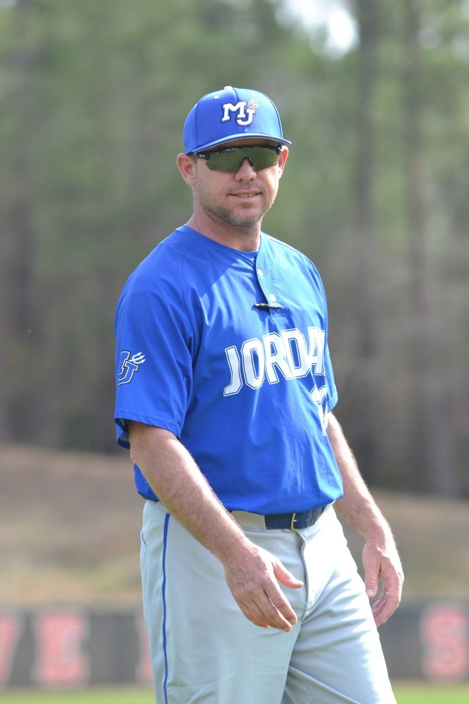 Shayne Carnes, Mortimer Jordan High School baseball coach smiles while walking on a baseball field and wearing his coaching uniform.