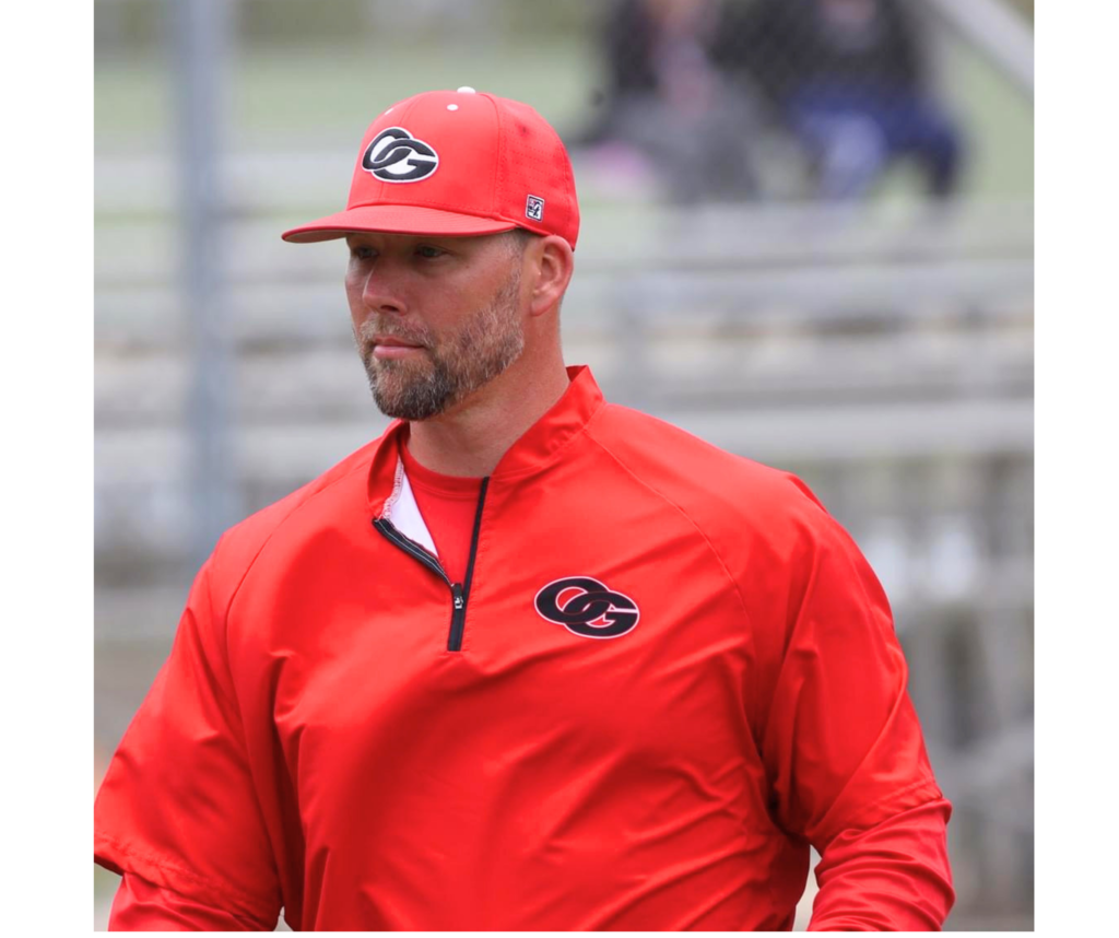 Jake Smith, Oak Grove High School baseball coach walks on a baseball field while wearing his coaching uniform.