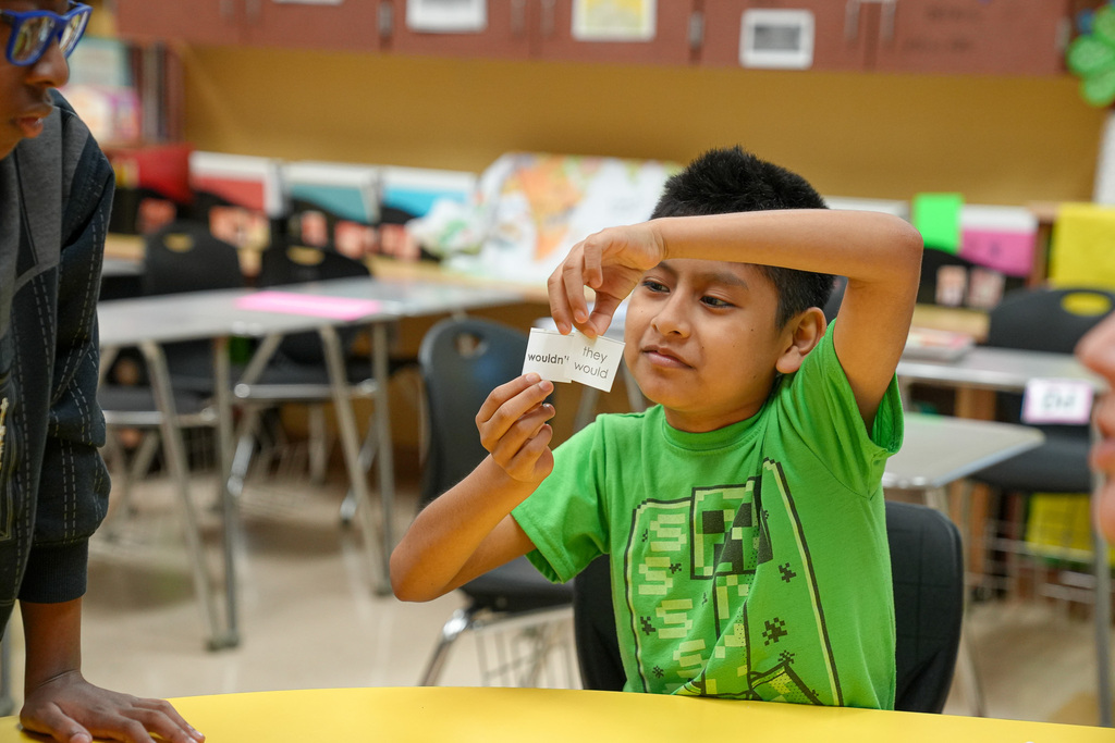 A student sits at a table and holds up pieces of paper with words printed on them.