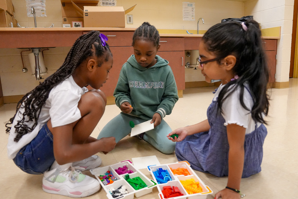 A group of students sit on the floor of a classroom and play with legos.