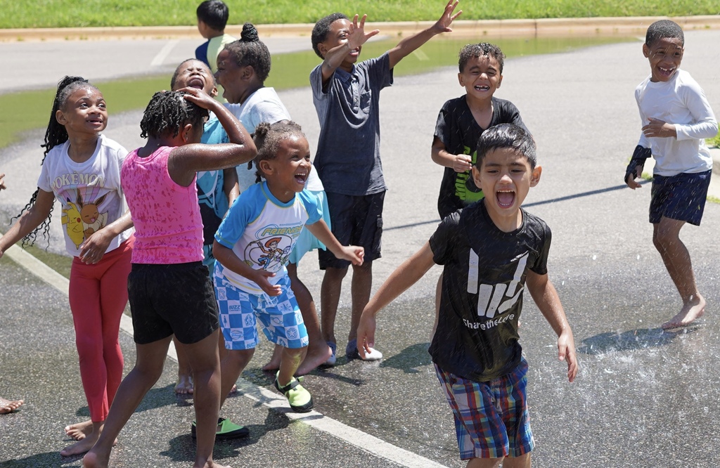 Students smile while playing in water outside in a parking lot.