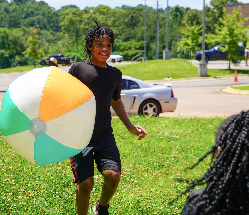 A student holds a large inflatable beach ball while playing outside on grass.