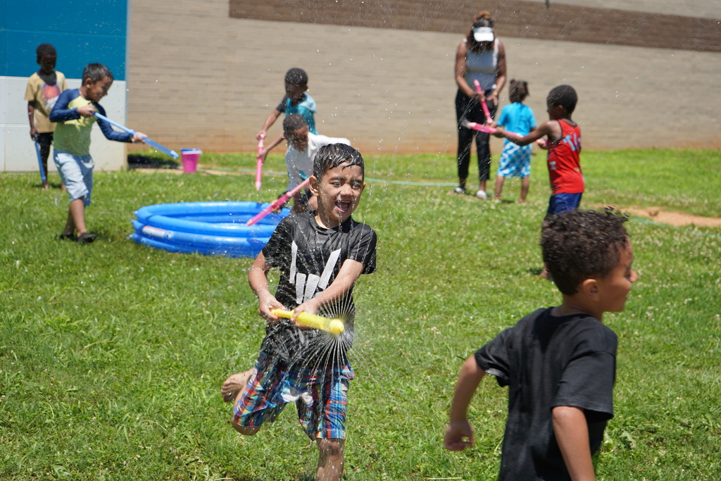 A student smiles while playing with a water gun outside.