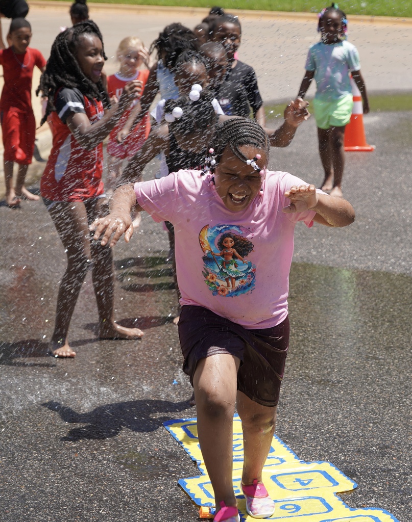 A student smiles while running through water being sprayed outside in a parking lot.