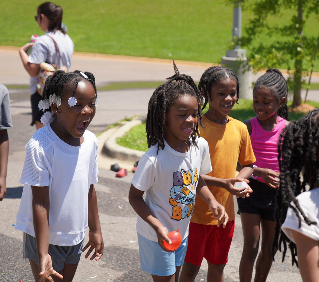 Students smile while playing with water balloons outside in a parking lot.